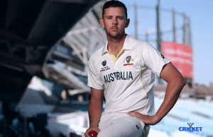 Cricket player in Australia team uniform, holding a ball, at a cricket ground.