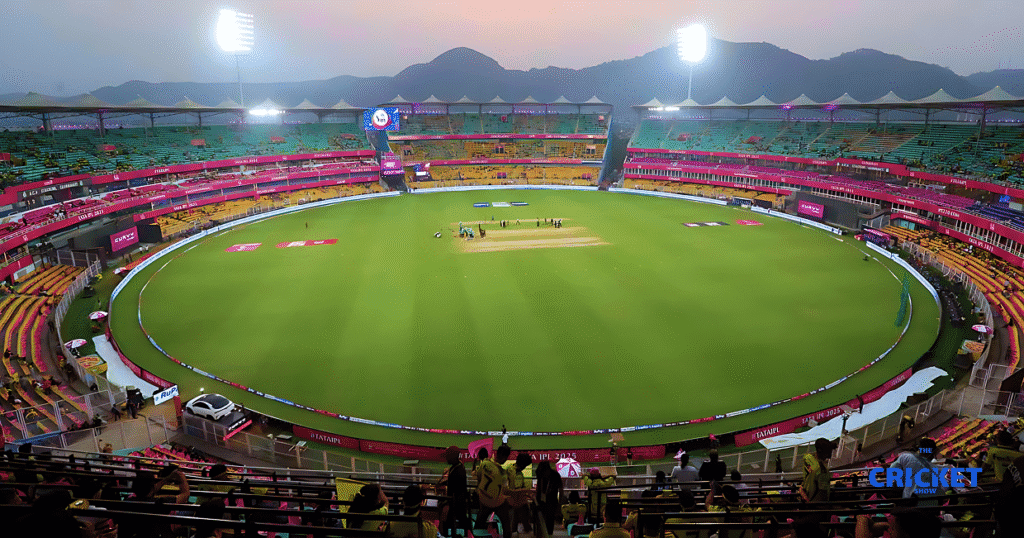 Guwahati Test stadium during evening with empty pitch and seating, illuminated for a cricket match.