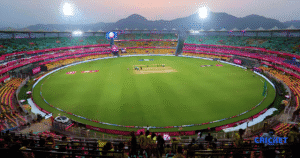 Guwahati Test stadium during evening with empty pitch and seating, illuminated for a cricket match.