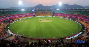 Guwahati Test stadium during evening with empty pitch and seating, illuminated for a cricket match.